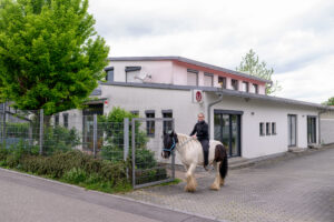 Praxisgebäude von außen. Tierärztin auf Pferd davor.